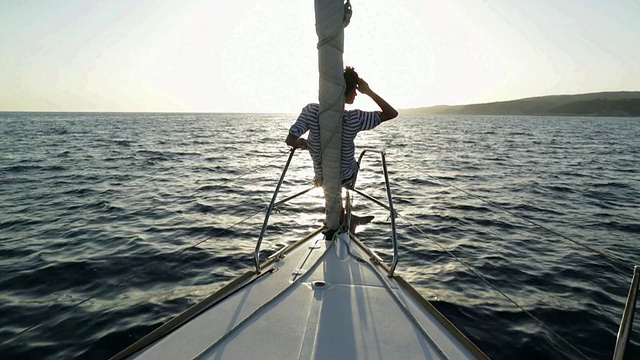 自信的年轻女子坐在船头，靠在船首的三角帆上，享受着微风，用手臂模仿海浪。视频素材