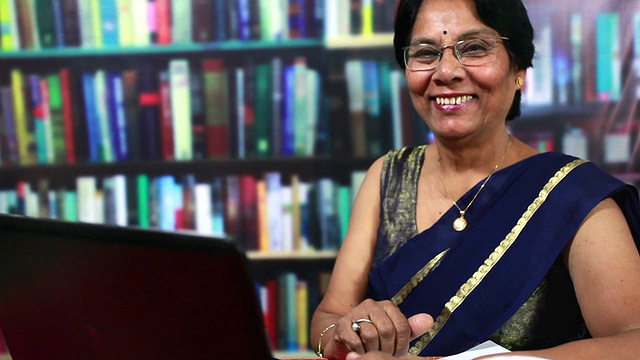 愉快的印度老年妇女在图书馆使用笔记本电脑视频素材