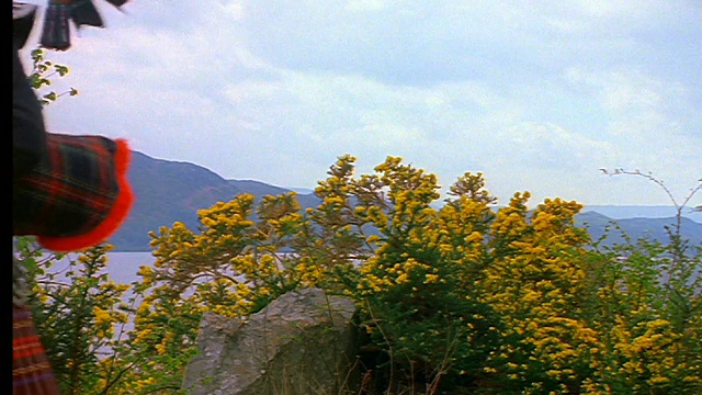 身穿苏格兰短裙、吹着风笛的男子走出屏幕/尼斯湖背景/苏格兰因弗内斯视频素材