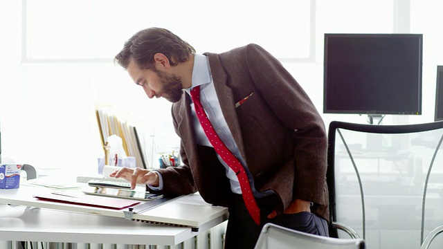 微软商人站在办公室的桌子上用数字平板电脑工作视频素材