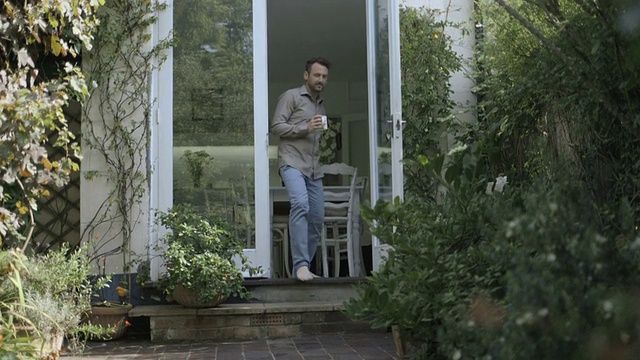 男人在屋外喝咖啡，朝花园走去。视频素材