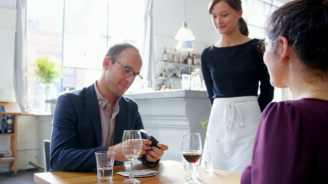微笑的服务员在餐厅给约会的情侣送账单视频素材