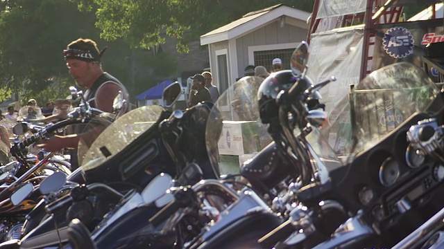 图为美国南达科塔州斯特吉斯摩托车拉力赛期间，三个男人一边聊天一边看着停在大街上的摩托车视频素材