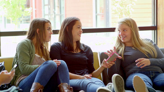 微软学生坐在高中的公共区域看智能手机视频下载