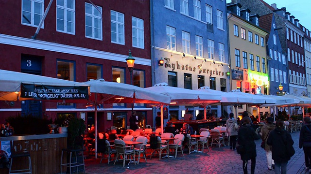 丹麦哥本哈根著名的尼哈芬，夜晚五颜六色的房屋和船只，还有成群结队的游客视频下载
