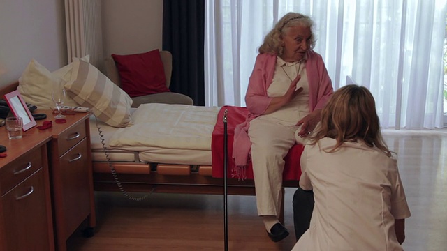 老女人坐在托儿所的床上和护士聊天。视频下载