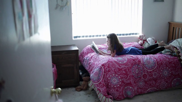 年轻的女孩从她的门往外偷看，然后躺在床上看书视频素材
