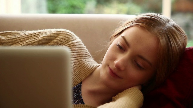 女孩躺在沙发上用笔记本电脑。视频素材