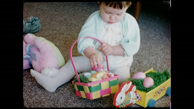 20世纪50年代，一个女婴坐在铺着地毯的客厅地板上玩着复活节彩蛋、复活节兔子和篮子视频素材