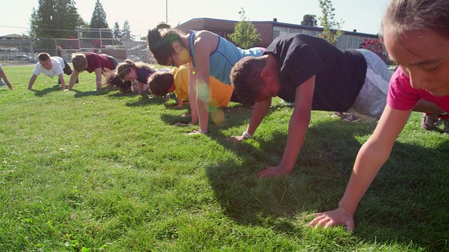 在学校旁边的草地上上体育课的时候，一群微笑着做俯卧撑的孩子视频素材