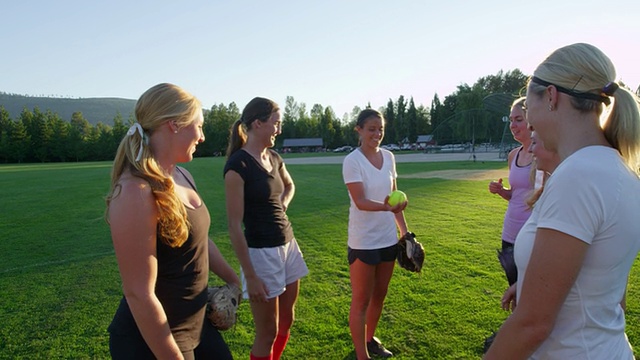 MS SLO MO组微笑女子垒球运动员抛球后，在球场上练习在夏天的晚上视频下载