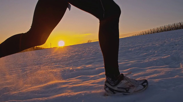 SLO MO慢跑者在夕阳下的雪中跋涉视频素材