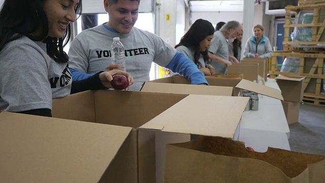 不同的志愿者在食品银行把捐赠的食物整理进盒子里视频素材