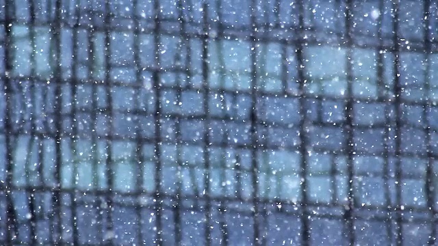 厚厚的雪花飘落，蓝色玻璃建筑作为背景。视频下载