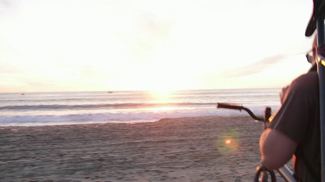 一个年轻人背着他的自行车在海滩上看日落的海洋。视频素材