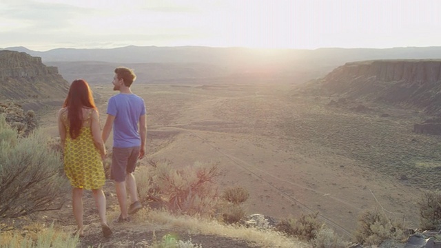 图女士微笑的夫妇手牵着手走在小路上俯瞰沙漠峡谷在日落视频素材