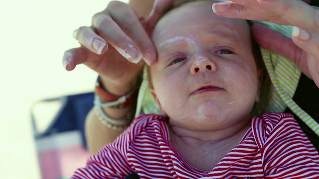 美国乔治亚州圣西蒙斯岛，母亲给宝宝涂抹防晒霜的照片视频素材