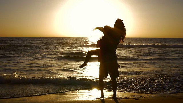 在美丽的海滩上，年轻的夫妇手牵着手，在夕阳下旋转。视频素材