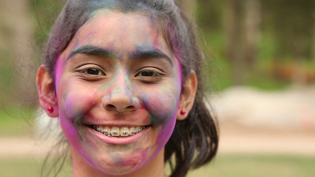 一个年轻女孩的肖像，脸上抹着彩粉微笑着。视频素材