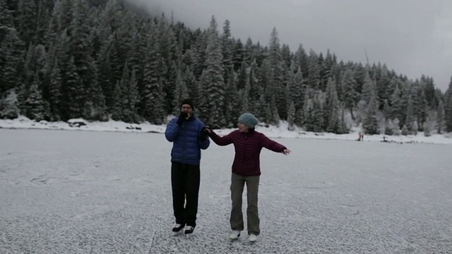 一对夫妇在蒙大拿州冰川公园的一个结冰的山湖上滑冰视频素材