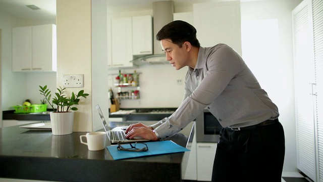 年轻男子在厨房使用笔记本电脑和智能手机视频素材