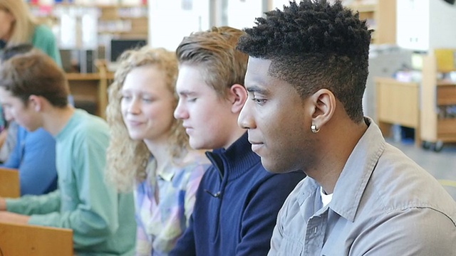 一名非裔美国青少年高中生走到一排电脑前坐下学习视频素材