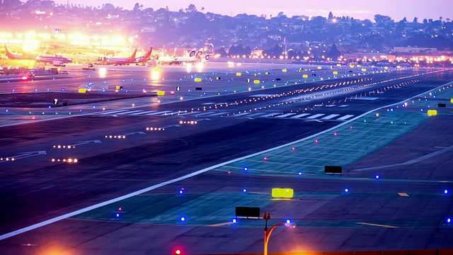 WS HA T/L机场跑道黄昏，跑道状态灯为蓝色，客机一个接一个降落，其他飞机在后面滑行，向美国加州圣地亚哥出发视频素材
