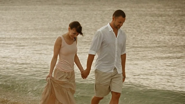 一对浪漫的情侣手牵着手在海边散步视频素材