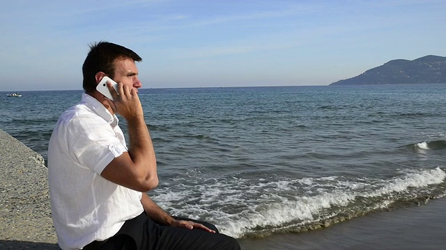 坐在海边打电话的男人。视频素材
