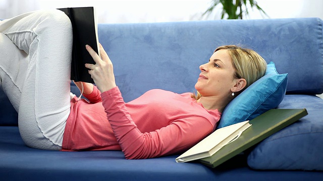年轻女子躺在沙发上看书。视频素材