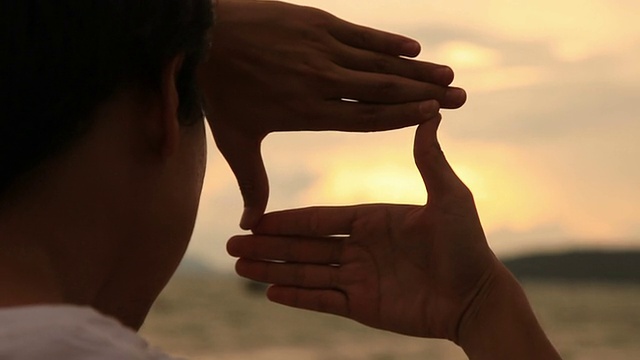 年轻男子在日落海滩上构图手架视频下载