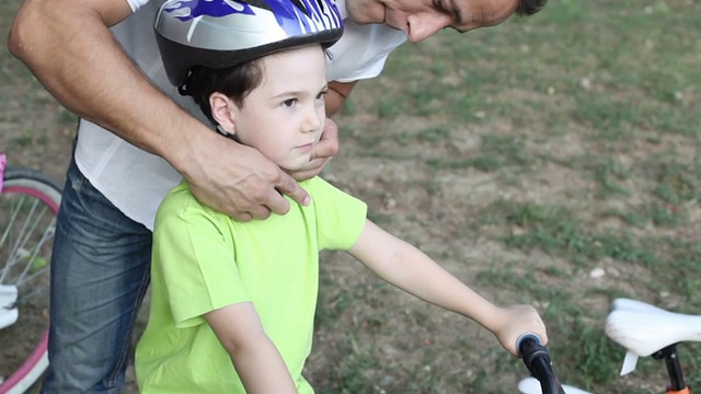 父亲协助孩子与自行车头盔。视频素材