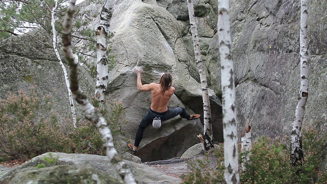 在枫丹地区，一个肌肉发达的年轻人正在攀登一块巨石视频素材