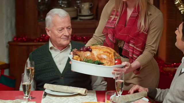 女人把火鸡带到圣诞餐桌上，家人鼓掌视频素材