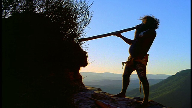 慢动作剪影男性土著演奏迪吉里杜管/山脉的背景/蓝山，澳大利亚视频素材