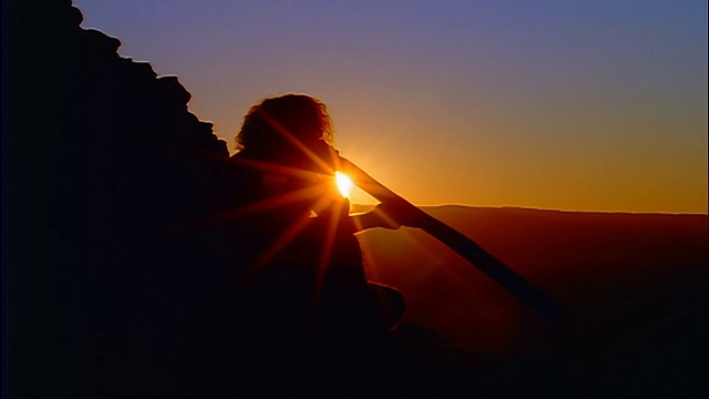 剪影坐在男性土著演奏迪吉里杜管/日落的背景/蓝山，澳大利亚视频素材