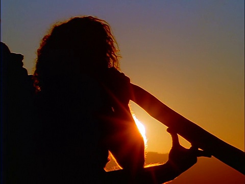 近剪影坐在男性土著演奏迪吉里杜管/日落的背景/蓝山，澳大利亚视频素材
