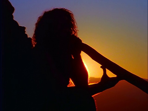 缩小剪影，坐在男性原住民演奏迪吉里杜管/日落的背景/蓝山，澳大利亚视频素材