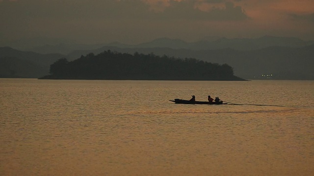 剪影:黄昏时分，渔民们乘坐长船在大坝上回家视频下载