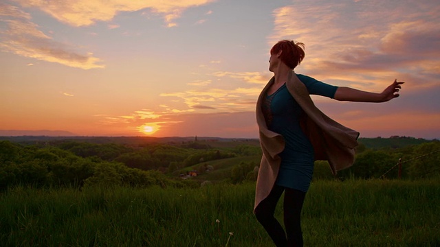 SLO MO快乐的女人在黄昏的草地上纺纱视频素材