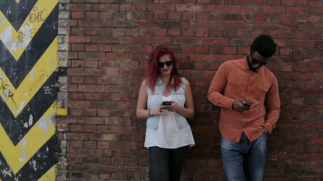 一对情侣靠在外面的砖墙上，看手机，发短信，调情视频素材