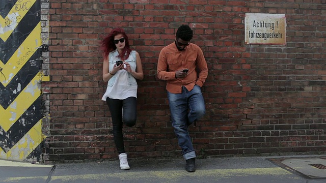 一对情侣靠在外面的砖墙上，看着手机，发短信，看着对方视频素材