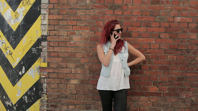 一个靠在砖墙上打电话的女人视频素材