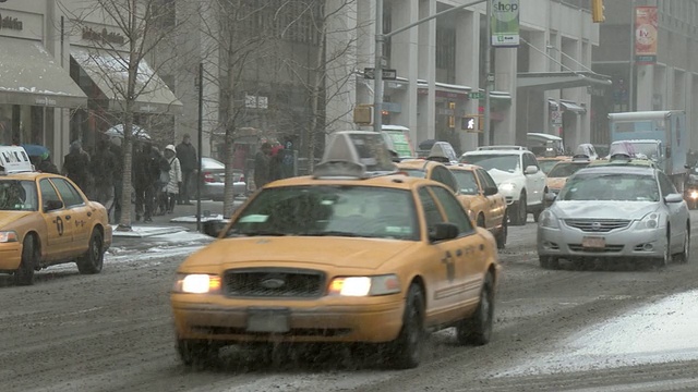 在一个大雪纷飞的冬日里，纽约街道上的车辆在移动。一名骑着助力车的送货员正在穿越。视频下载