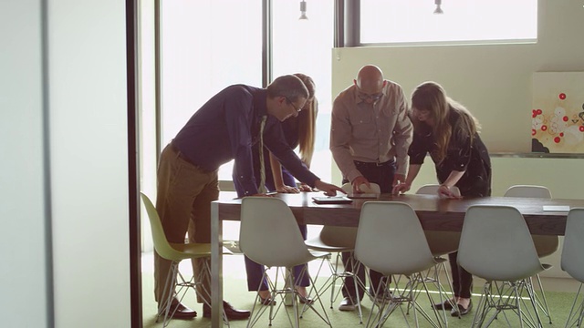 商务人士站在办公室会议室的桌子上，在非正式会议中讨论数字平板电脑上的项目视频下载
