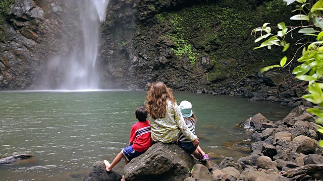 母亲和孩子们坐在岩石上观看秘密瀑布/怀鲁阿，考艾岛，夏威夷，美国视频下载