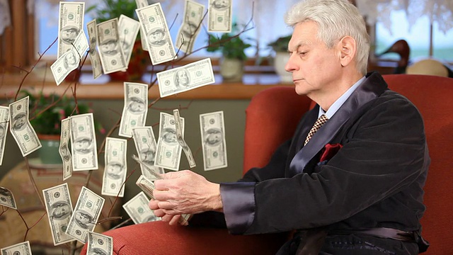坐在扶手椅上的百万富翁从钱树上捡100美元钞票视频下载