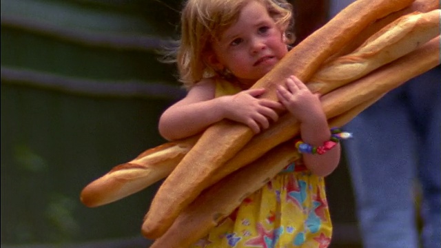 小女孩抱着长棍面包微笑着跑向照相机/法国巴黎视频下载