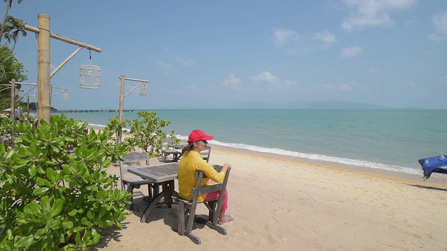 一个女人坐在海滩上看着一个卖海滩货的人视频素材