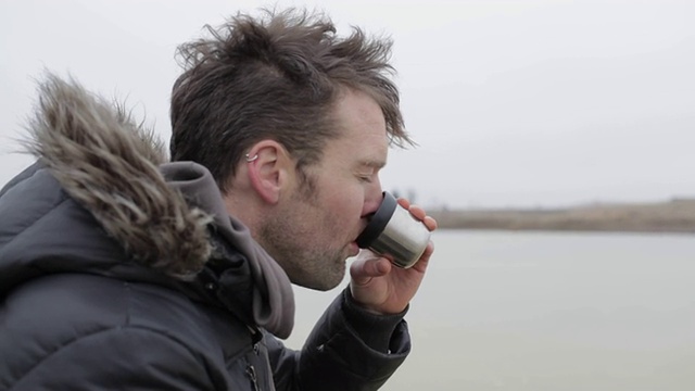 在美国蒙大拿州的乡下，一个年轻人在结冰的池塘上喝着热茶。视频素材